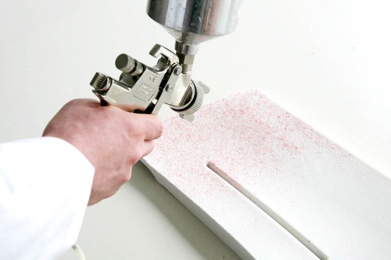 Sprühkleber wird mit Druckluftpistole auf ein Schaumstoffteil aufgetragen
